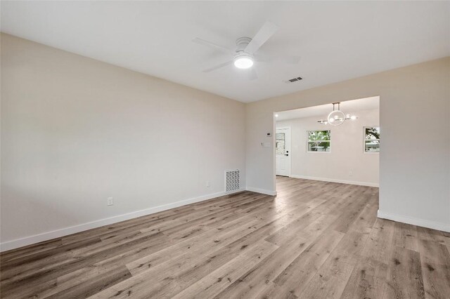 empty room with baseboards, visible vents, ceiling fan with notable chandelier, and light wood-style floors