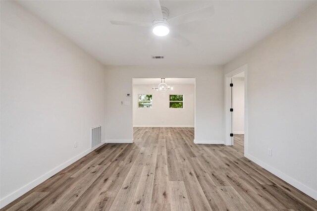 spare room featuring baseboards, ceiling fan with notable chandelier, light wood-style flooring, and visible vents