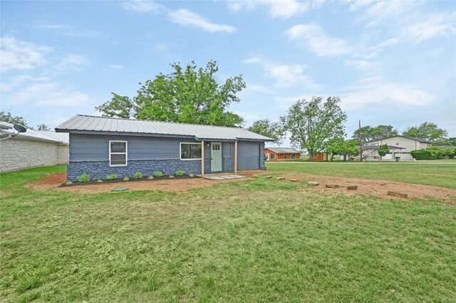 rear view of house featuring a yard, metal roof, and stone siding