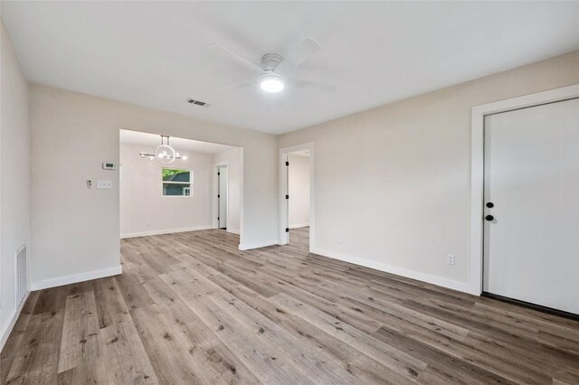 interior space with baseboards, ceiling fan with notable chandelier, wood finished floors, and visible vents