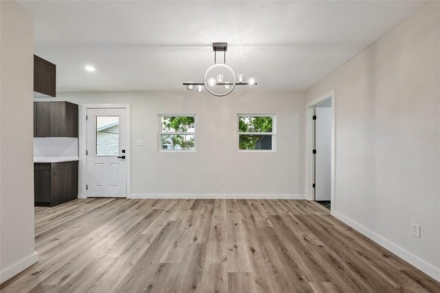 unfurnished dining area with an inviting chandelier, a wealth of natural light, and light wood-style flooring