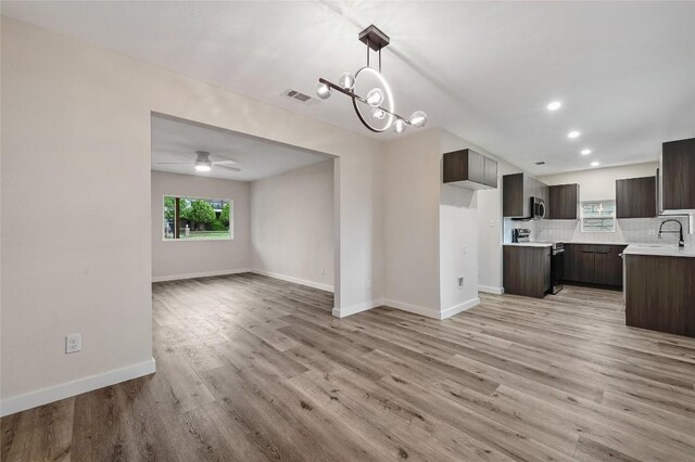 interior space featuring baseboards, visible vents, ceiling fan with notable chandelier, and light wood-type flooring