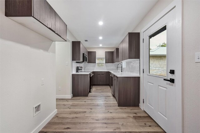 kitchen with decorative backsplash, appliances with stainless steel finishes, dark brown cabinets, a sink, and light wood finished floors