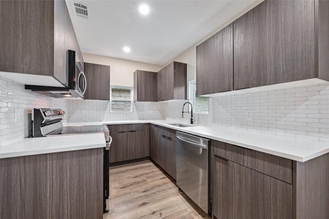 kitchen with appliances with stainless steel finishes, a sink, light countertops, decorative backsplash, and modern cabinets