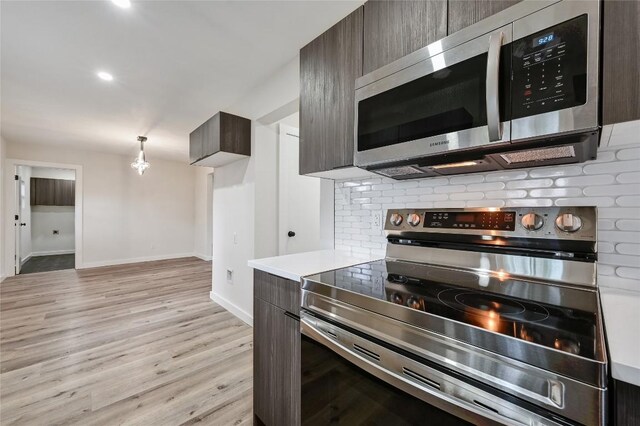 kitchen with light wood-type flooring, dark brown cabinets, light countertops, baseboards, and stainless steel appliances