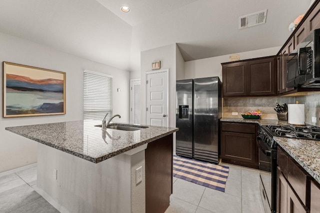 kitchen with visible vents, a sink, light stone counters, black gas range, and stainless steel fridge
