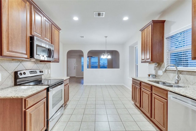 kitchen with appliances with stainless steel finishes, a sink, arched walkways, decorative backsplash, and visible vents