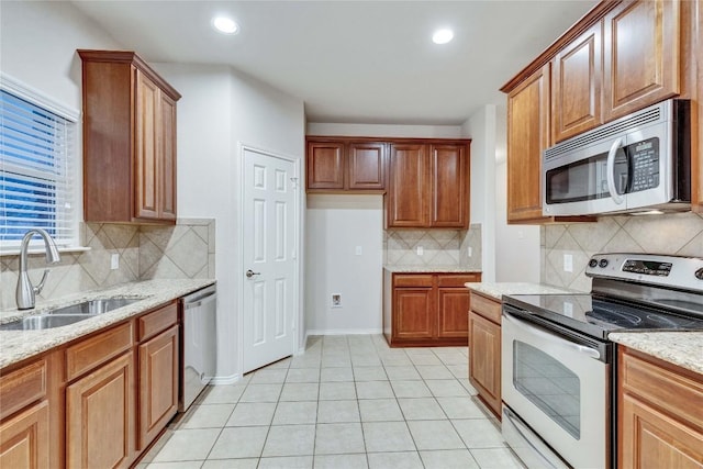 kitchen with appliances with stainless steel finishes, light stone counters, a sink, light tile patterned floors, and backsplash