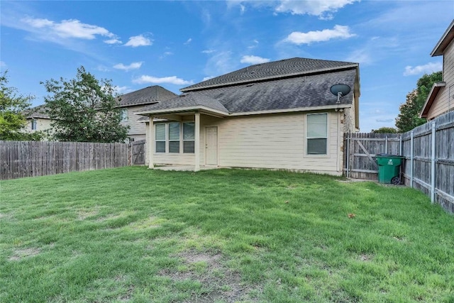 back of property with a lawn, a shingled roof, and a fenced backyard