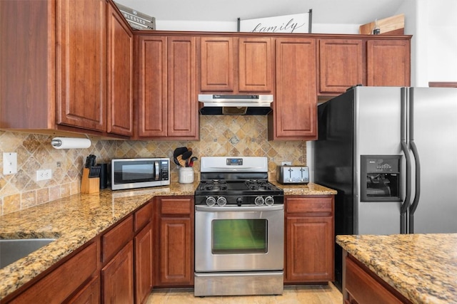 kitchen featuring under cabinet range hood, appliances with stainless steel finishes, decorative backsplash, and light stone counters