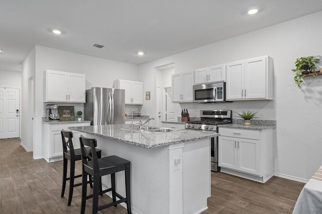 19216 Bear Grass Dr, Elgin, TX 78621 - kitchen featuring appliances with stainless steel finishes, dark wood-type flooring, a kitchen breakfast bar, white cabinetry, and a center island with sink