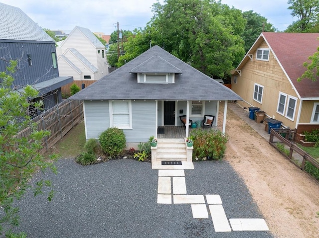 bungalow-style home with roof with shingles, fence, and covered porch
