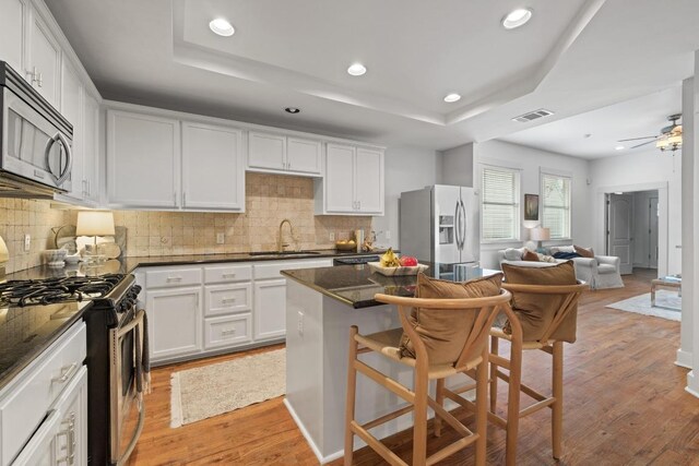 kitchen with a sink, appliances with stainless steel finishes, tasteful backsplash, and a tray ceiling