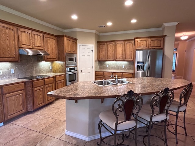 1005 Fort Davis St, Georgetown, TX 78633 - kitchen featuring appliances with stainless steel finishes, a sink, under cabinet range hood, brown cabinets, and a kitchen breakfast bar