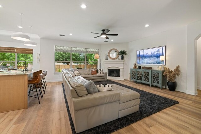living room featuring ceiling fan, light wood finished floors, arched walkways, a glass covered fireplace, and recessed lighting