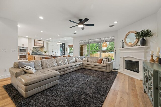 living room featuring a glass covered fireplace, ceiling fan, light wood-type flooring, and visible vents