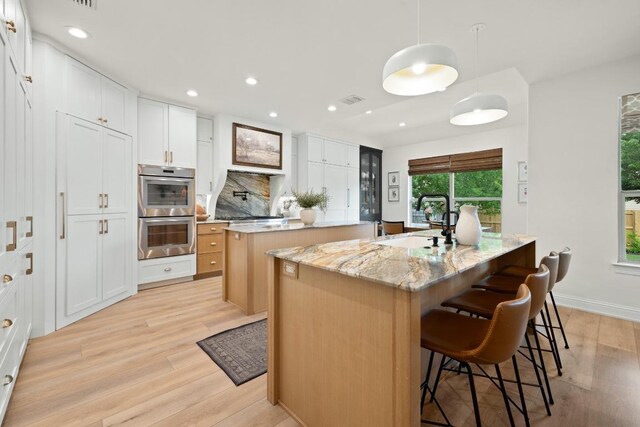kitchen featuring a sink, double oven, a kitchen breakfast bar, light wood-type flooring, and a center island with sink