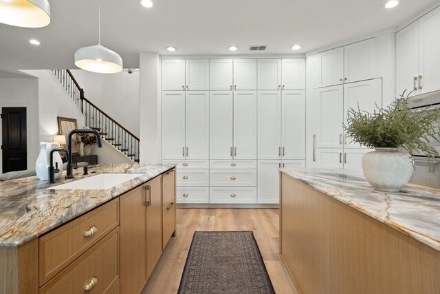 kitchen with white cabinets, a sink, light wood finished floors, recessed lighting, and visible vents