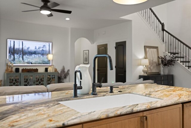 kitchen featuring light stone countertops, ceiling fan, a sink, arched walkways, and recessed lighting