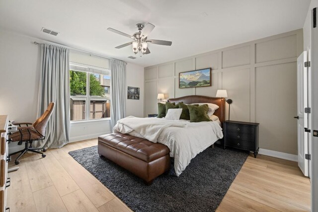 bedroom featuring light wood-style floors, a ceiling fan, a decorative wall, and visible vents