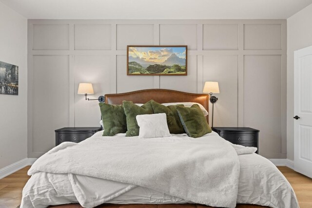 bedroom with baseboards, a decorative wall, and light wood finished floors