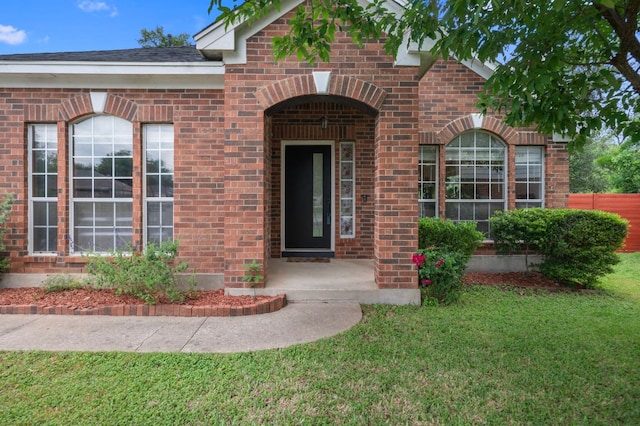 doorway to property featuring brick siding, fence, and a yard