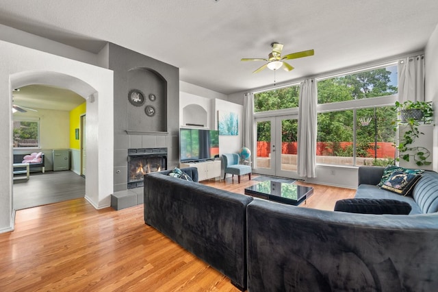 living room featuring a tiled fireplace, ceiling fan, french doors, and light wood finished floors