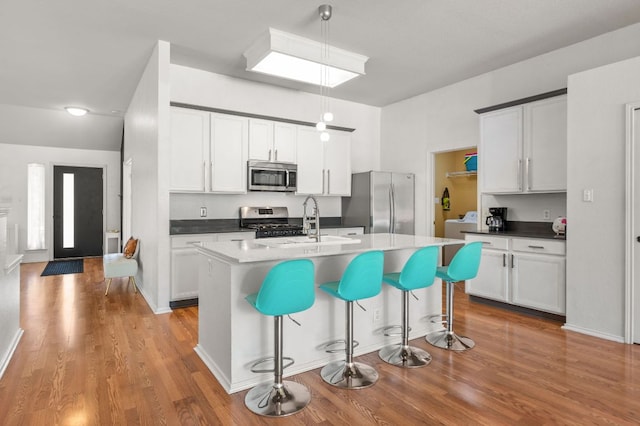 kitchen with wood finished floors, a breakfast bar, white cabinetry, a sink, and appliances with stainless steel finishes