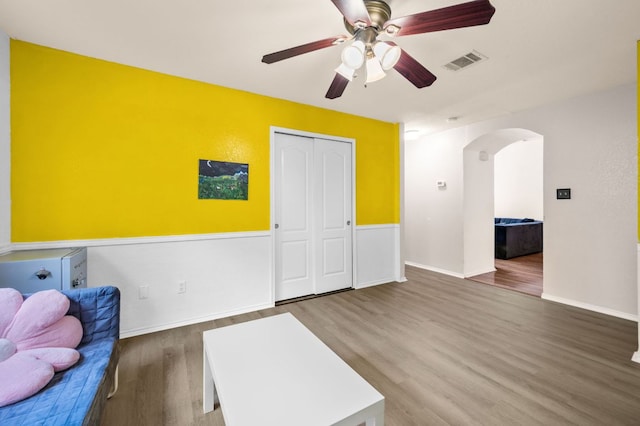interior space featuring ceiling fan, visible vents, arched walkways, wood finished floors, and baseboards