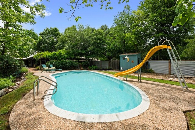 view of swimming pool featuring fence, a water slide, a fenced in pool, a playground, and an outdoor structure