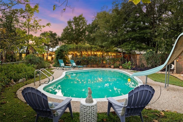 pool at dusk with a water slide, a fenced backyard, a patio area, and a fenced in pool