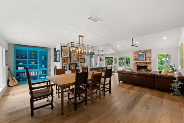 dining area featuring visible vents, vaulted ceiling, a brick fireplace, light wood-type flooring, and recessed lighting