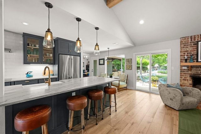 kitchen featuring a breakfast bar area, high end refrigerator, light stone counters, glass insert cabinets, and vaulted ceiling with beams