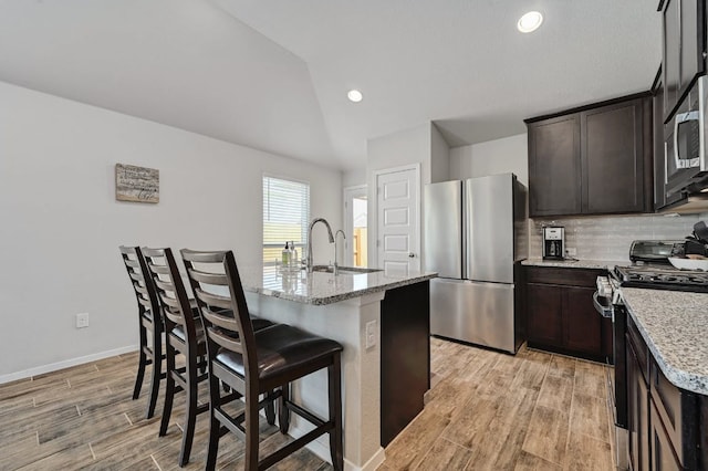 155 Lyndon Dr, San Marcos, TX 78666 - kitchen featuring dark brown cabinets, appliances with stainless steel finishes, light stone counters, a kitchen breakfast bar, and light wood-type flooring