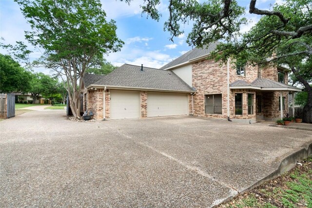 view of front facade featuring a garage, driveway, roof with shingles, and brick siding