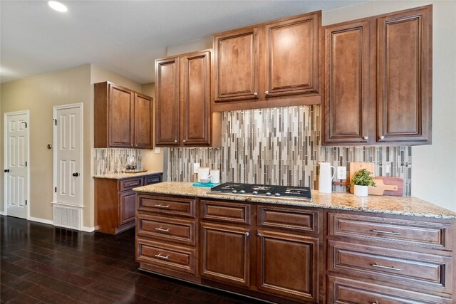 kitchen featuring light stone counters, dark wood finished floors, baseboards, stainless steel gas stovetop, and tasteful backsplash