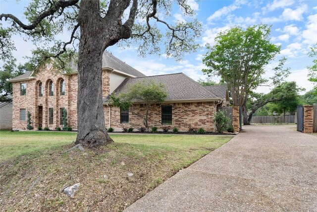 view of front of home featuring brick siding, a shingled roof, fence, and a front yard