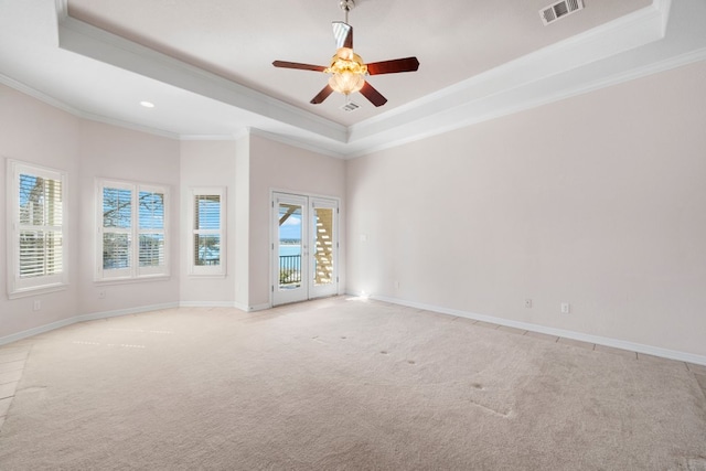 empty room featuring a raised ceiling, ceiling fan, light carpet, and visible vents