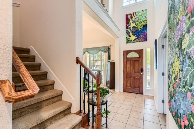 foyer featuring baseboards, a towering ceiling, light tile patterned flooring, and stairway