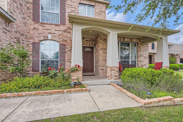 view of exterior entry featuring a porch and brick siding