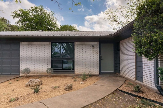 view of exterior entry with an attached garage, metal roof, and brick siding