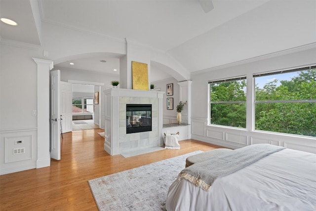 bedroom with ornamental molding, lofted ceiling, a tiled fireplace, arched walkways, and light wood finished floors