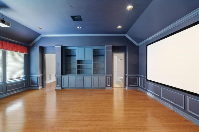 cinema with ornamental molding, wainscoting, a decorative wall, light wood-style floors, and vaulted ceiling
