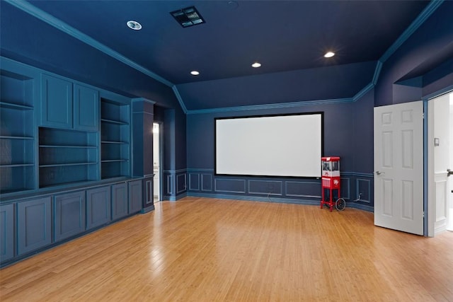cinema room featuring crown molding, light wood finished floors, a decorative wall, and a wainscoted wall