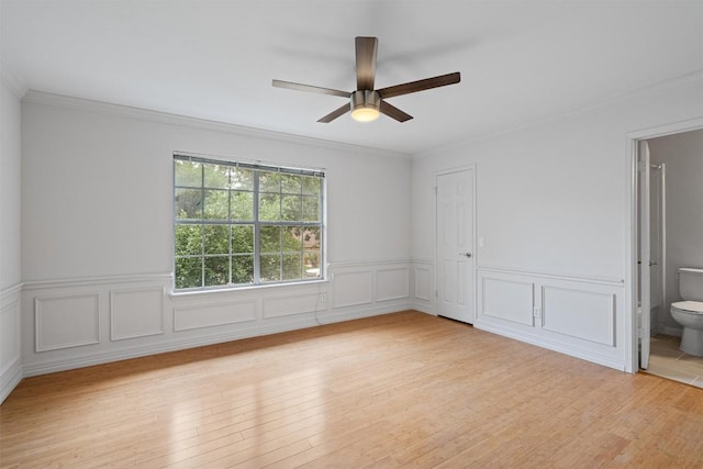 unfurnished bedroom featuring ornamental molding, light wood finished floors, ensuite bath, and wainscoting