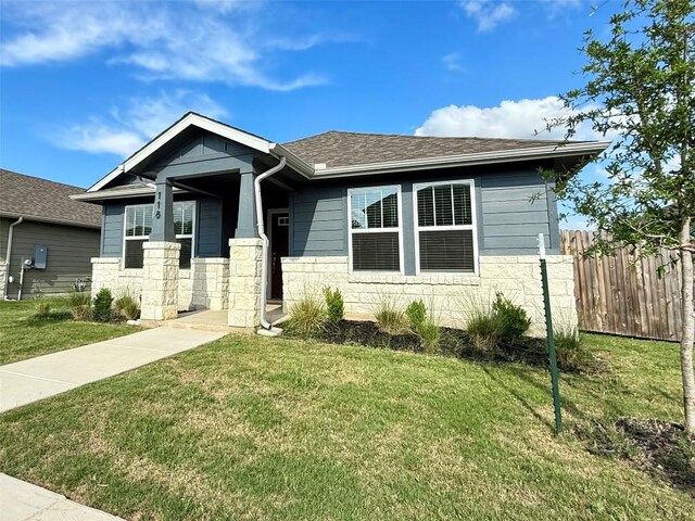 view of front facade featuring a shingled roof, fence, a front yard, and stone siding