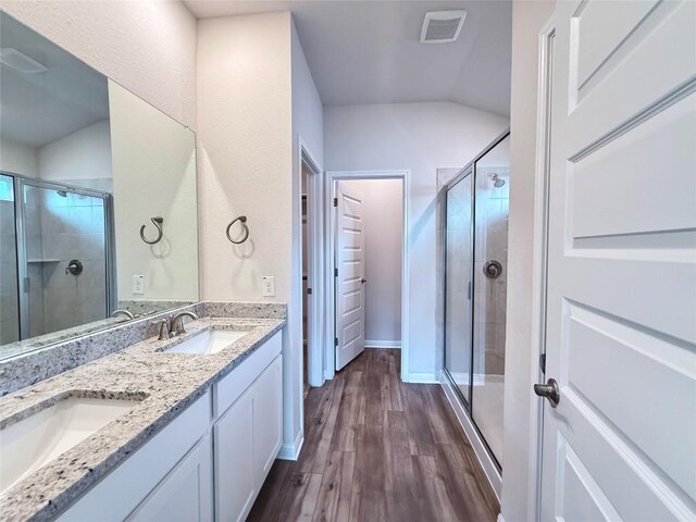 bathroom featuring wood finished floors, double vanity, a sink, and a stall shower