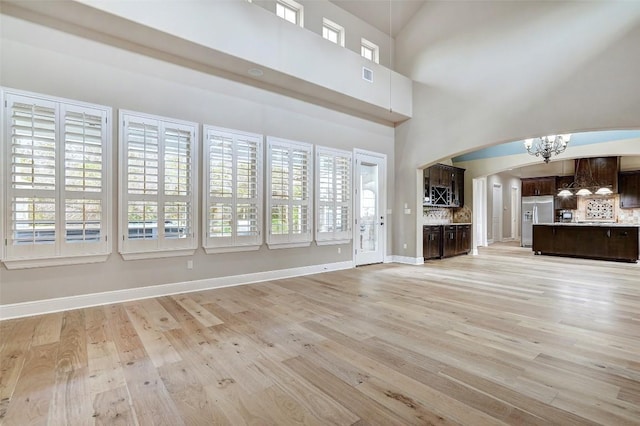 423 Bella Montagna Cir, Austin, TX 78734 - unfurnished living room featuring a chandelier, light wood-style floors, arched walkways, and healthy amount of natural light