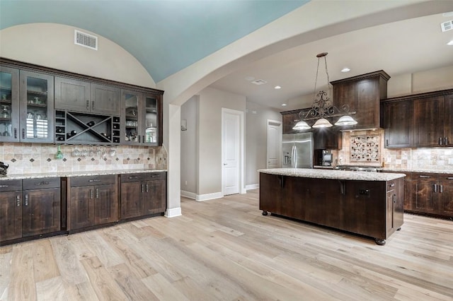 kitchen with dark brown cabinetry, stainless steel fridge with ice dispenser, arched walkways, light wood-type flooring, and tasteful backsplash