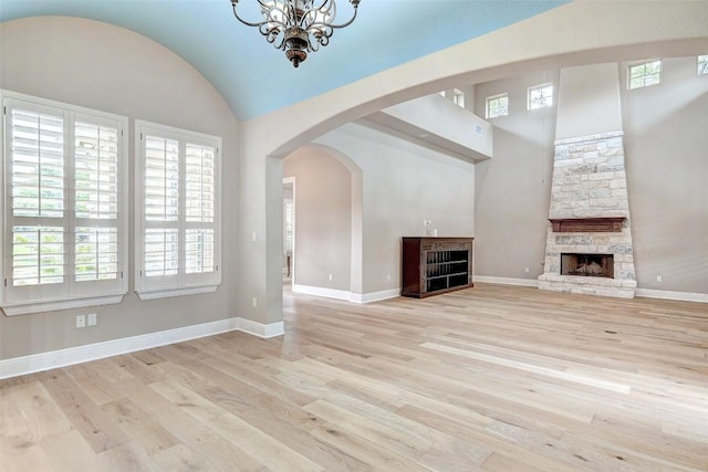 423 Bella Montagna Cir, Austin, TX 78734 - unfurnished living room with light wood-type flooring, a stone fireplace, healthy amount of natural light, arched walkways, and lofted ceiling